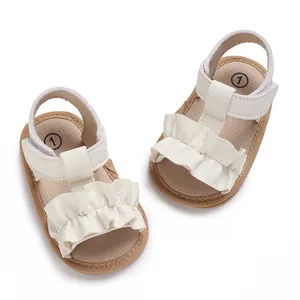 Primer plano de sandalias blancas para bebé con volantes y suelas suaves para caminar.