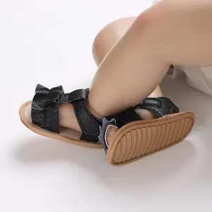 Detalle de sandalias para bebé niña con suela de goma ondulada y textura de cuero negro