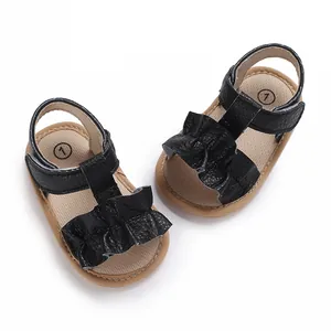 Primer plano de sandalias negras para bebé con tiras rizadas y suela de goma blanda para verano