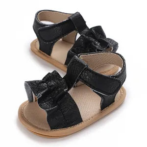Detalle de sandalias negras para bebé con suela de goma blanda y diseño de ondas.