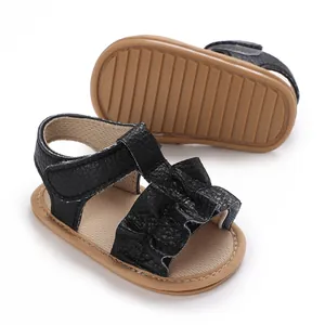 Detalle de sandalias negras para bebé con tiras de volantes y suelas de goma marrón