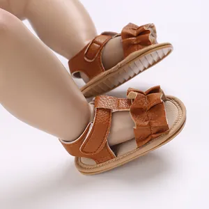 Primer plano de sandalias marrones para bebé con tira de volantes y suela de goma suave