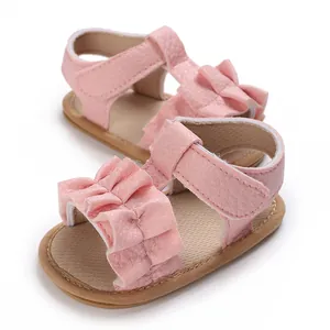 Primer plano de sandalias rosas para bebé con volantes decorativos y piel sintética texturizada.