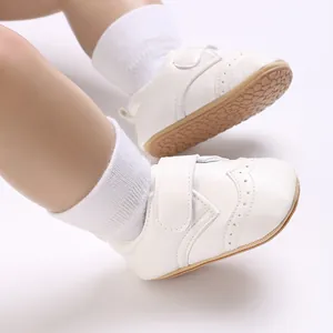 Close-up detail of white faux leather baby shoes with brogue pattern and rubber soles