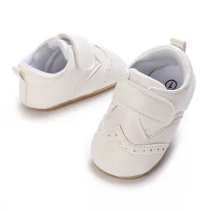 Detailed view of white leather infant boy walking shoes with Velcro strap and brogue pattern
