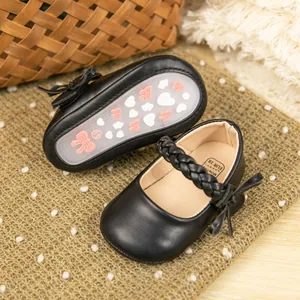 Nahaufnahme schwarzer Babyschuhe aus PU-Leder mit geflochtenem Riemen und Schleife