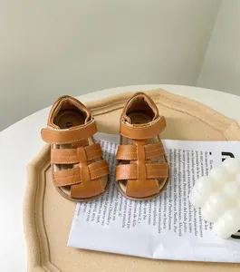 Détail de sandales romaines marron pour tout-petits avec semelle souple et surpiqûres blanches.