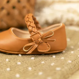 Detaillierte Nahaufnahme brauner PU-Leder Babyschuhe mit Schleife und Flechtriemen