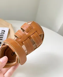 Gros plan sur les sandales romaines en cuir marron pour fille avec surpiqûres blanches