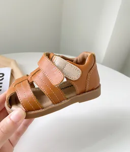 Gros plan d'une sandale marron en cuir pour bambin avec coutures contrastées.