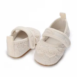 Primer plano de zapatos de princesa de encaje crema para bebé con bordado de flores.
