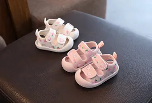 Vue détaillée de sandales de bébé blanches et roses avec imprimés fraises sur fond sombre.