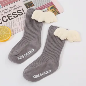 Detail of baby ribbed socks featuring plush angel wings and non-slip 'KIDS SOCKS' grip.