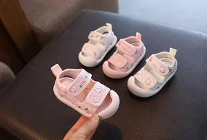 Gros plan de sandales roses et blanches pour bébé avec motifs fraise et petit ours.