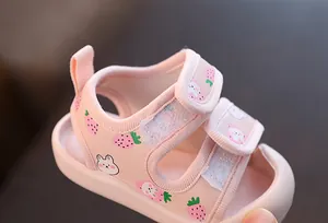 Détail de sandales roses pour bébé fille avec motifs fraises et fermetures velcro.