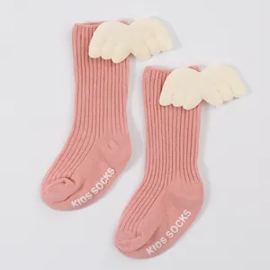 Detail view of pink ribbed baby socks with white plush angel wings and non-slip soles.