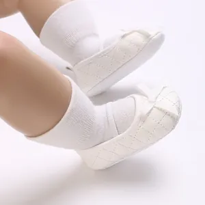 Close-up detail of white quilted soft sole baby shoes featuring a delicate ribbon bow