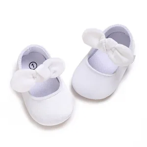 Top view detail of white baby girl baptism shoes with large bow and soft sole.