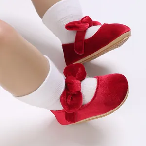 Close-up of red velvet baby girl shoes featuring a large bow and soft tan sole