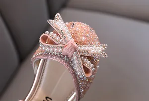 Primer plano de zapatos de princesa rosas para niñas con lazo de perlas y pedrería