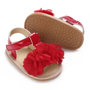 Primer plano de sandalias rojas para bebé niña con flores de tela grandes y suela blanda.
