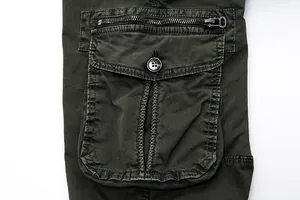Detailed view of dark green military cargo pants pocket featuring zipper and button flap.