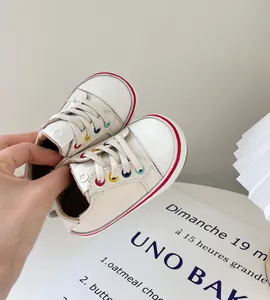 Detailaufnahme cremefarbener Baby-Lauflernschuhe mit bunten Ösen und weichen Sohlen.