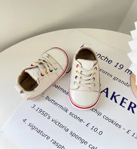 Detailaufnahme weißer Lauflernschuhe für Babys mit bunten Ösen auf stilvollem Hintergrund