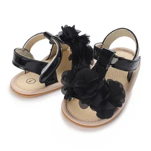 Detalle de sandalias negras para bebé con flores decorativas y suela blanca blanda.