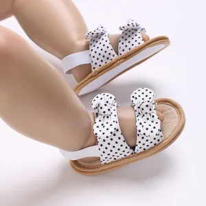 Primer plano de sandalias de lunares para bebé niña con lazos y suela blanda de verano.