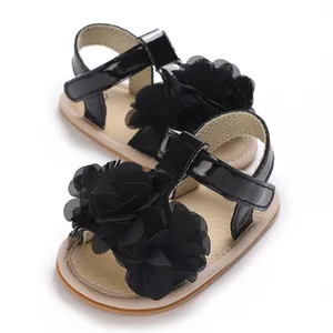 Primer plano de sandalias negras para bebé con flores de gasa y suelas blandas.