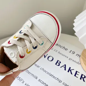 Modische weiße Leder-Lauflernschuhe für Kleinkinder mit bunten Ösen und weicher Sohle.