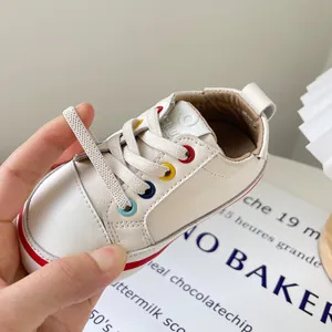 Weiße minimalistische Lauflernschuhe für Babys mit bunten Ösen und weichen Sohlen