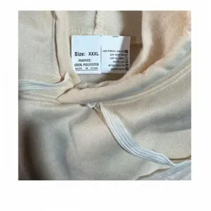 Detalle de etiqueta de lavado en sudadera beige, 100% poliéster y talla XXXL, de felpa