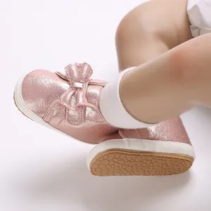 Vue rapprochée de chaussures de marche pour bébé rose pailleté avec nœud et semelle souple.