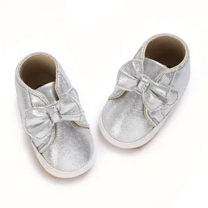 Vue détaillée de chaussures argentées pour bébé avec nœud et semelle souple blanche