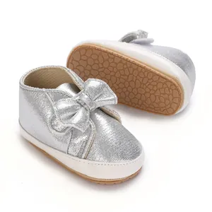 Gros plan sur des chaussures argentées pour bébé avec noeud scintillant et semelle souple.