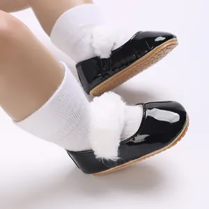 Dettaglio scarpe neonato in pelle verniciata nera con pompon di pelliccia sintetica bianca.