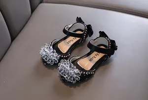 Nahaufnahme schwarzer Prinzessinnenschuhe mit elegantem Kristallblumendekor und Pailletten.