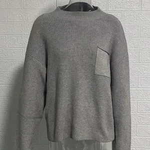Gros plan d'un pull en maille gris à col rond avec une poche de poitrine détaillée