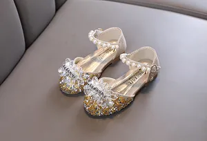 Nahaufnahme goldene Prinzessinnenschuhe für Mädchen mit Kristallblume und Perlenband