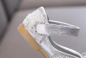 Detailopname van zilveren glitter prinsessenschoenen met strasstenen en parels.
