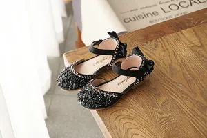 Detailed view of black girl's rhinestone performance shoes with bow and ankle strap