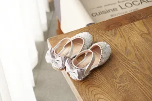 Close-up of sparkling silver rhinestone girl's shoes with elegant bows on a wooden surface