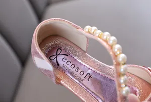 Détail d'une chaussure de princesse rose pailletée avec bride perlée et étiquette.