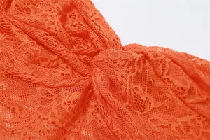 Detailed macro view of vibrant orange floral lace fabric with intricate knot design