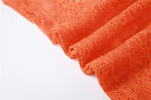 Close-up of bright orange floral lace fabric showing intricate mesh texture