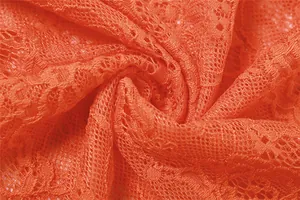Close-up macro view of vibrant orange sheer lace fabric texture with floral patterns