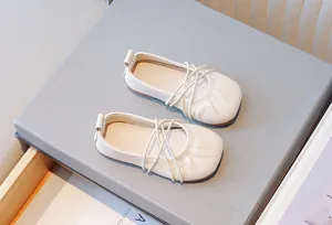 Primer plano de elegantes bailarinas crema para niñas con detalle de tiras cruzadas