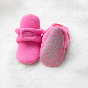 Primer plano de patucos de forro polar rosa para bebé con suelas antideslizantes suaves.